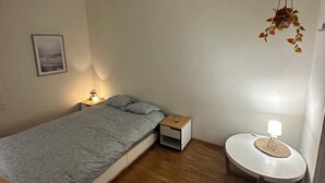 A bedroom with a bed, bedside tables, a small round table with a lamp, and a hanging plant. - Central and comfortable apartment for two or three people (Lausanne)