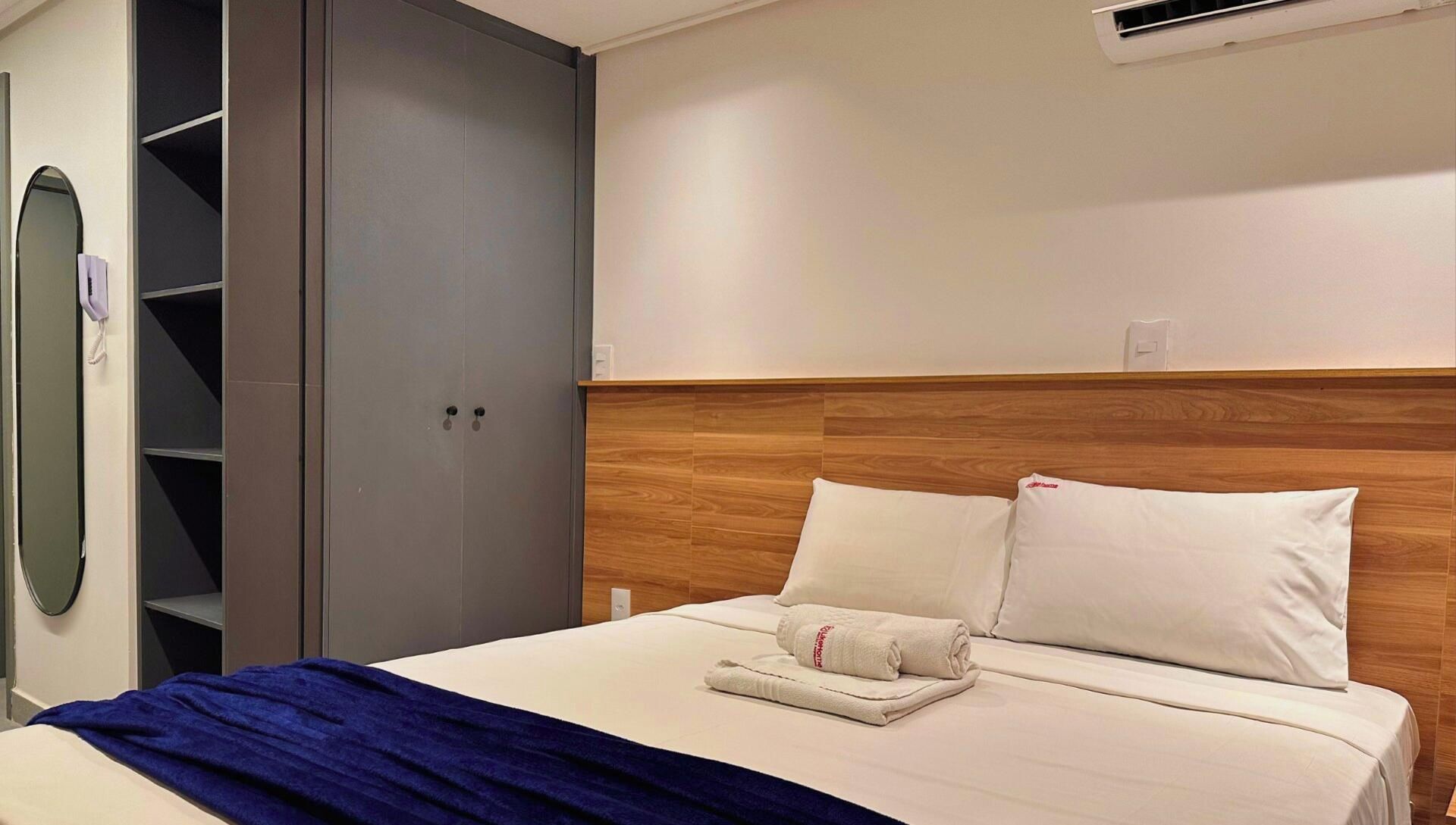 A hotel room with a bed, a wooden headboard, a wardrobe, and a mirror.