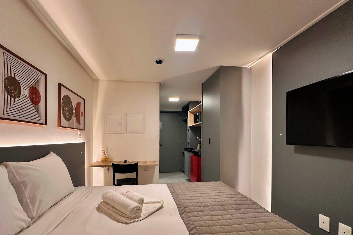 Habitació d'hotel amb un llit, una taula de treball, una cadira, un televisor fixat a la paret i obra d'art a la paret.