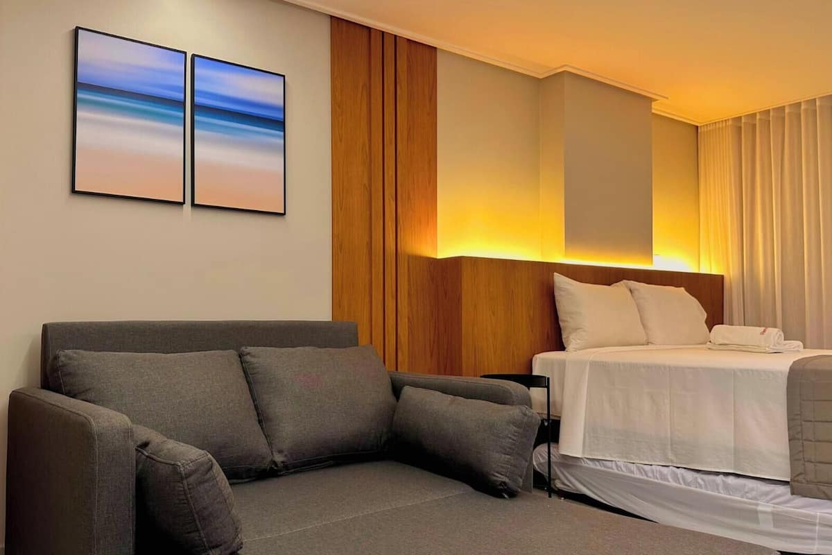 Habitación de hotel con sofá, cama, mesita de noche y dos cuadros colgados en la pared.