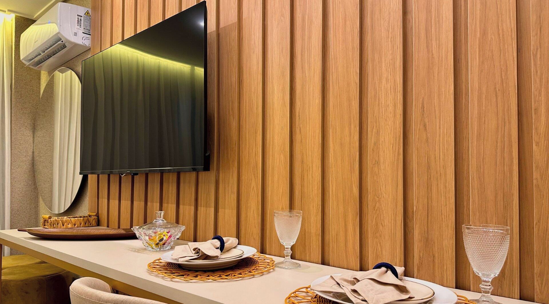 A room with a flat-screen TV mounted on a wooden wall, a table set with plates, glasses, and a decorative bowl.