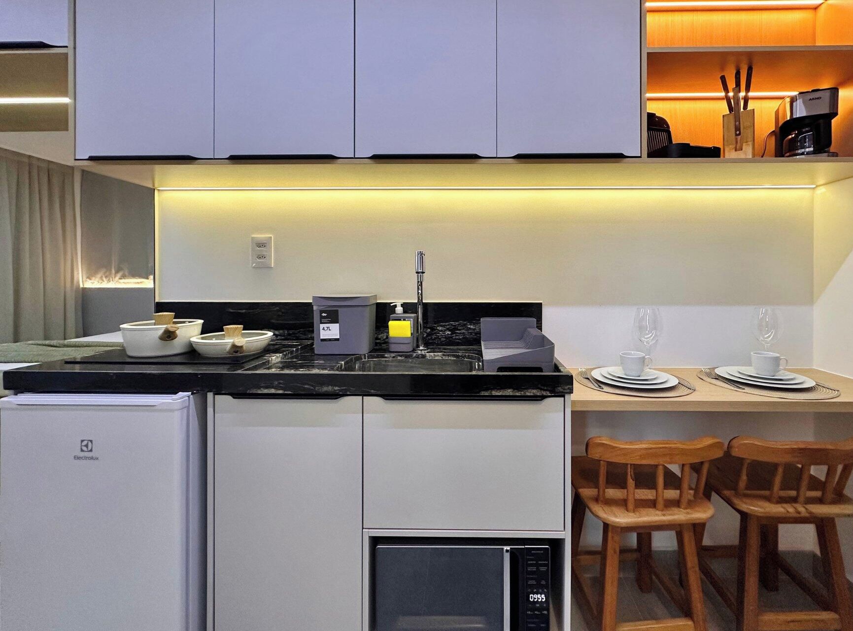 A compact kitchen with a refrigerator, stove, and microwave. There is a dining area with a table set for two and two wooden chairs.