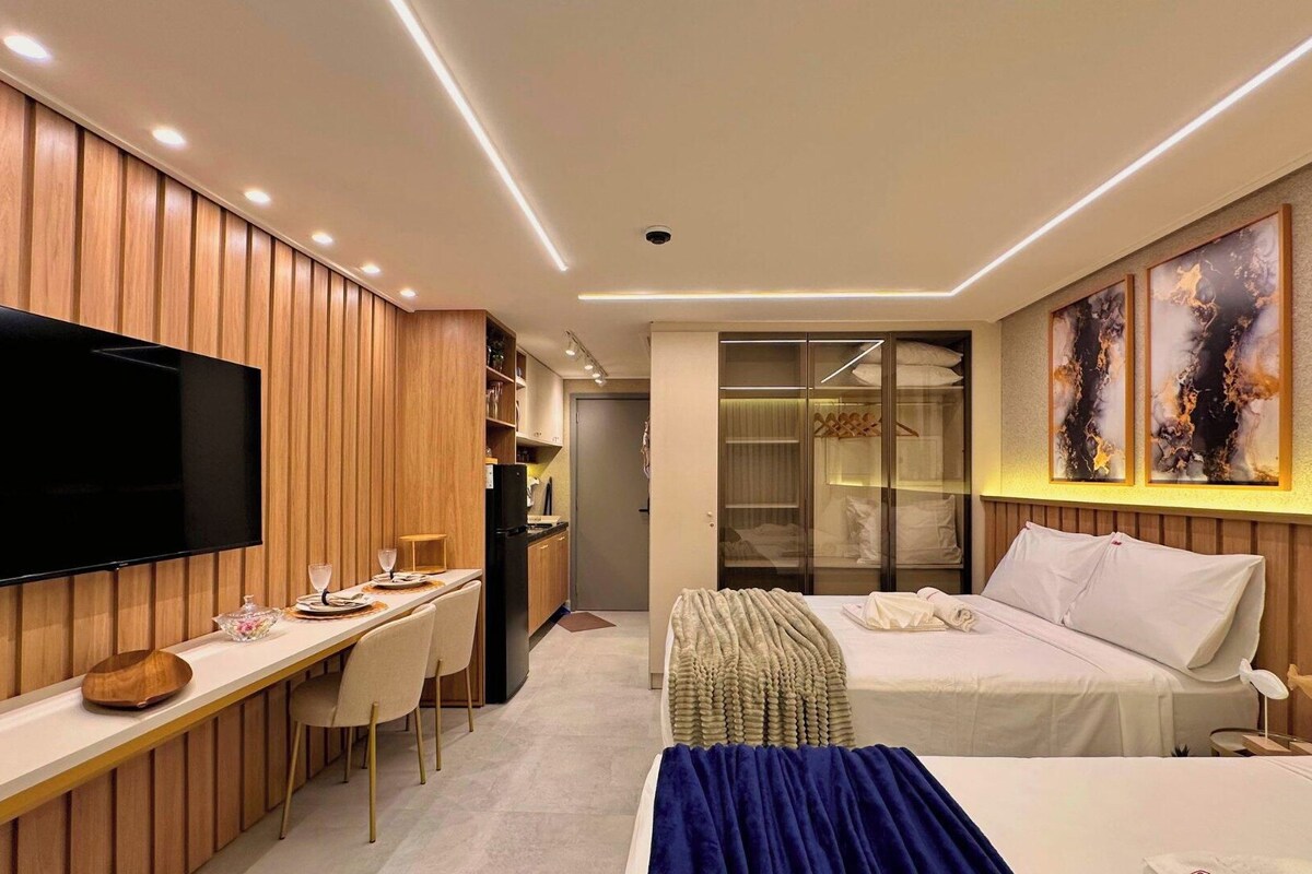 Una habitación de hotel moderna con televisión de pantalla plana, una cama, un escritorio con sillas y un vestidor.