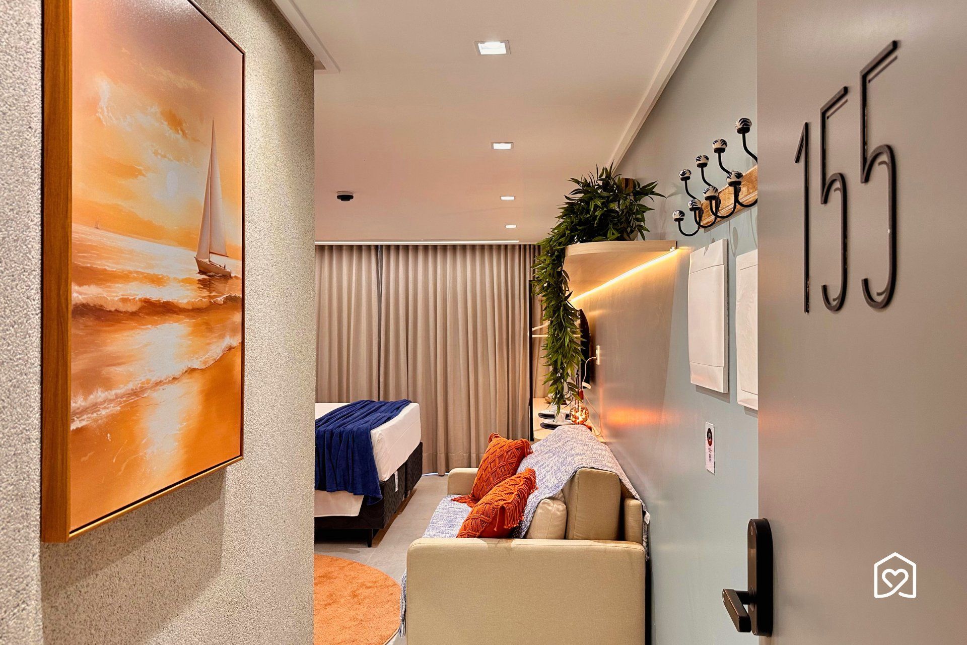 A hotel room with a bed, a seating area, a wall-mounted plant, and a painting of a sailboat.