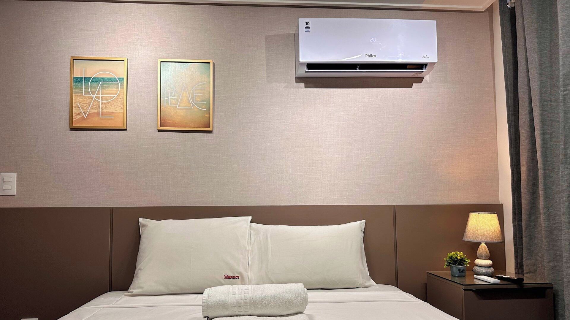 Quarto de hotel com cama, ar condicionado fixado na parede e duas obras de arte emolduradas.