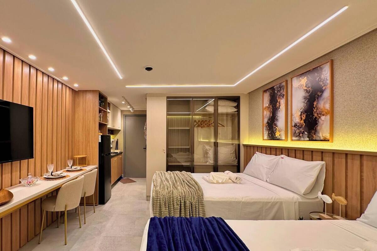 Una habitación de hotel moderna con televisión de pantalla plana, un escritorio con sillas, una cama y un vestidor.