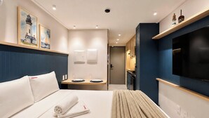 Ein Hotelzimmer mit einem Bett, einem Fernseher, einem kleinen Tisch mit Gläsern und einer Tür zu einem Badezimmer.