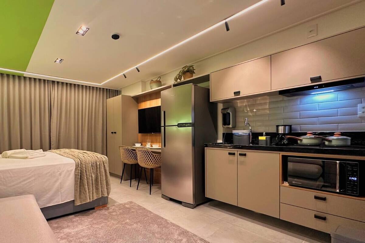 Una habitación de hotel moderna con una cama, una pequeña zona de comedor, una kitchenette y una pared de acento verde.