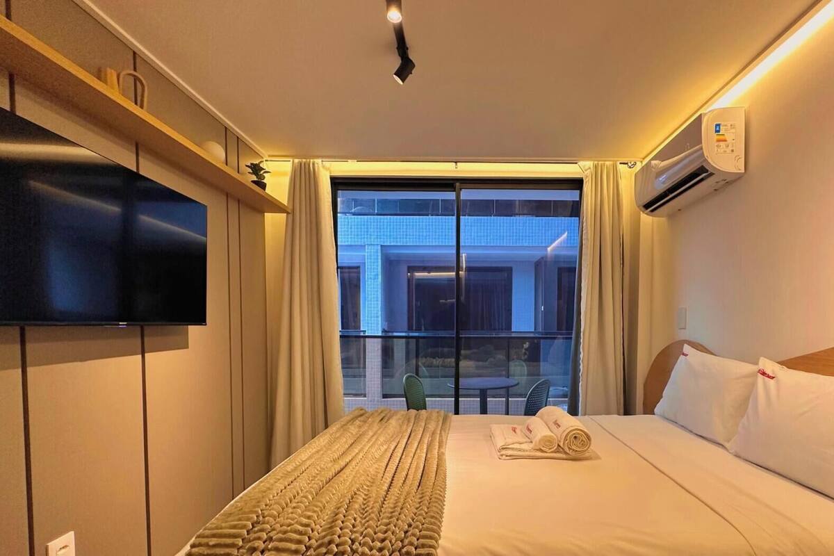 Una habitación de hotel con una cama, televisión, ventana con cortinas y aire acondicionado.