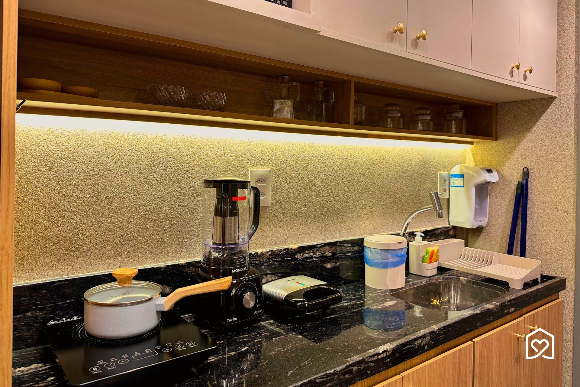 A kitchen with a stove, a coffee maker, a sink, and a soap dispenser.