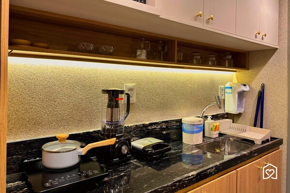 Una cocina con estufa, cafetera, lavamanos y dispensador de jabón.