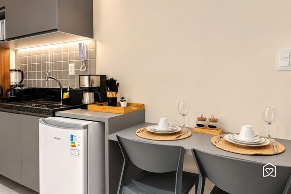 A modern kitchen with a refrigerator, stove, and various appliances. There is a dining area with a table set for two, including plates, glasses, and cutlery. - Hit Cabo Branco IV - LikeHome (João Pessoa)