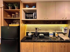 Una cocina compacta con un refrigerador negro, un microondas, una cafetera y un lavamanos.