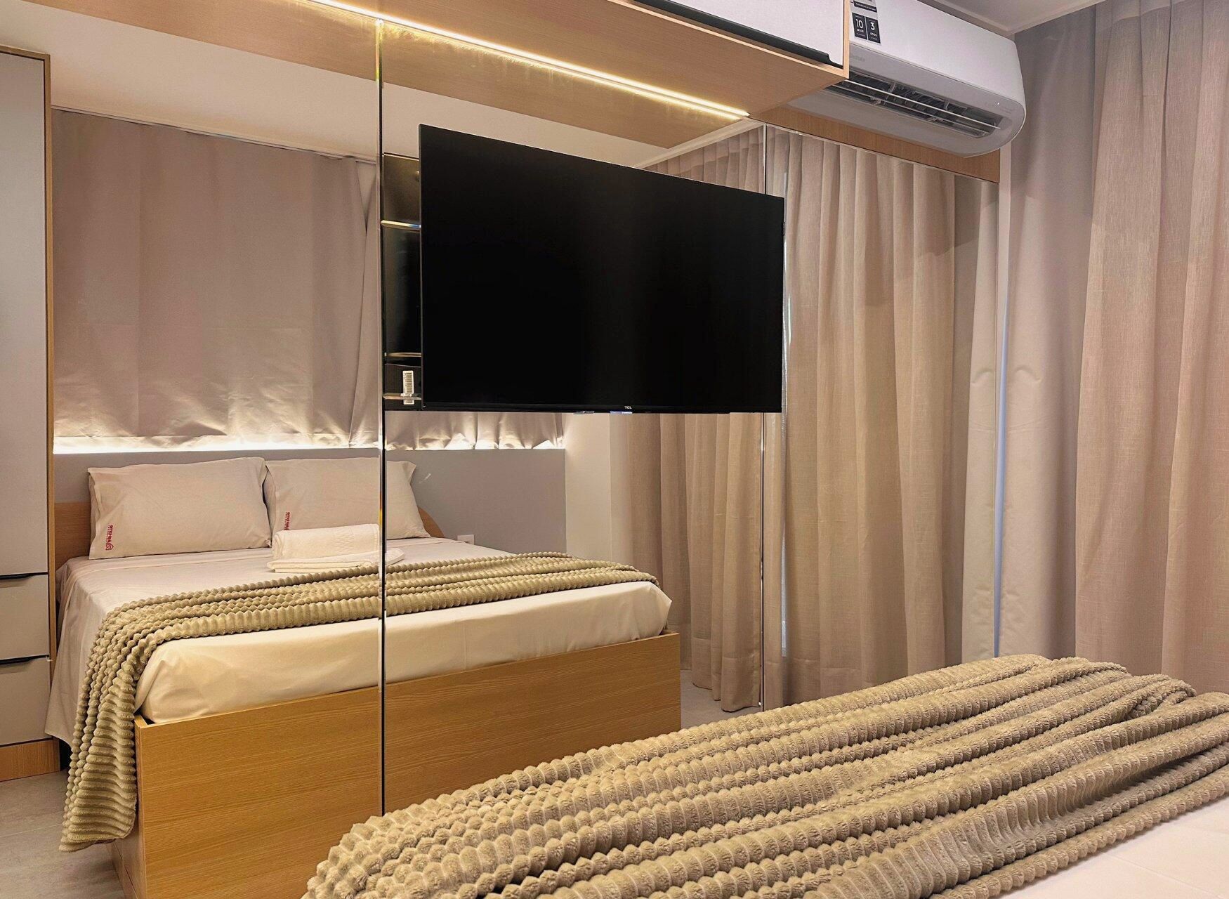 A modern bedroom with a bed, a television mounted on a wall, and an air conditioning unit.