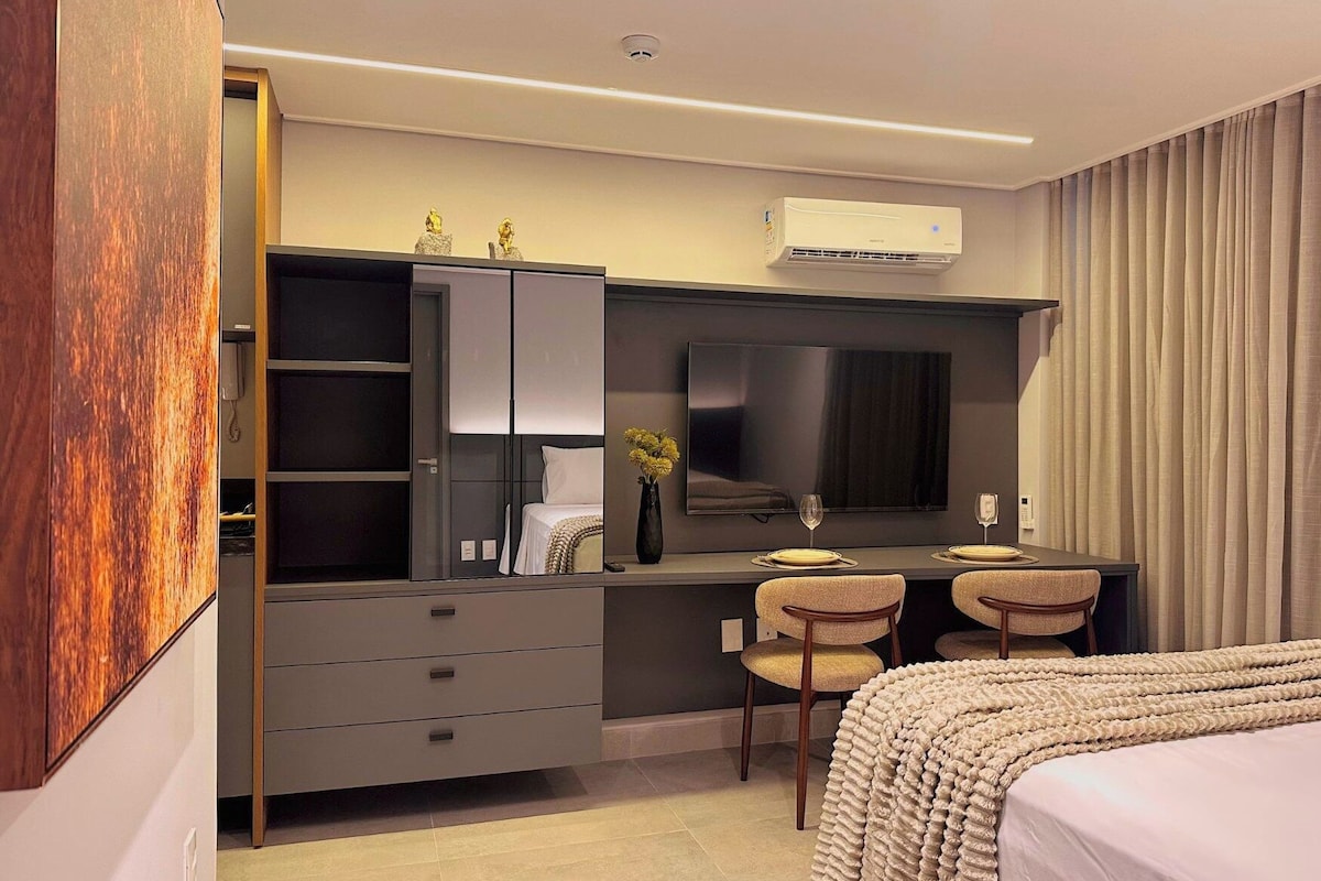 Una habitació d'hotel moderna amb un llit, una taula de treball amb dues cadires, una televisió de pantalla plana i un armari.