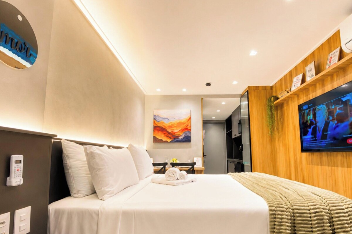 Habitación de hotel con cama, televisión, un cuadro y aire acondicionado de pared.