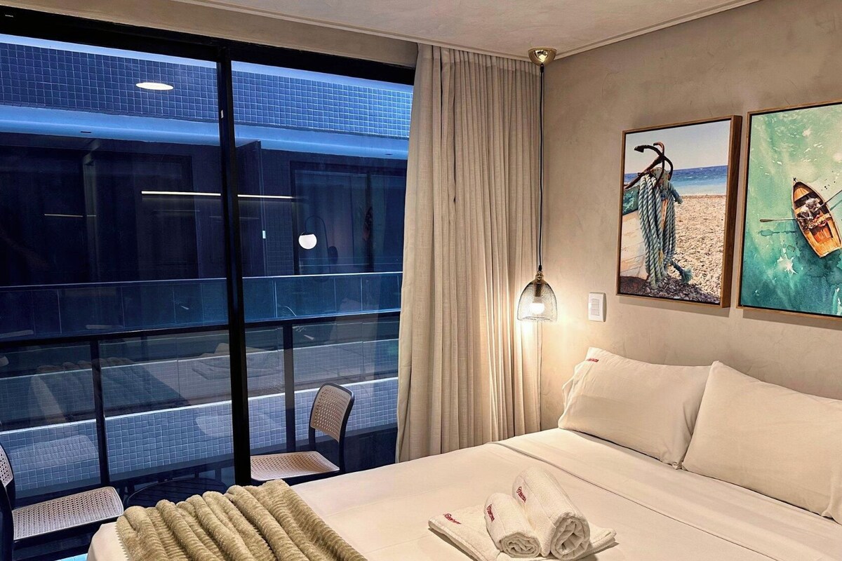 Habitación de hotel con cama, una silla, una mesa y vista a un edificio a través de una puerta de vidrio.