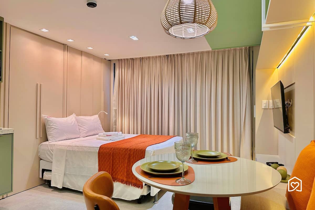 Una habitación de hotel moderna con una cama, una mesa de comedor para dos personas y un amplio ventanal con cortinas.