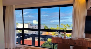 Una habitación de hotel con un ventanal grande, una cama, un escritorio con sillas y un televisor.