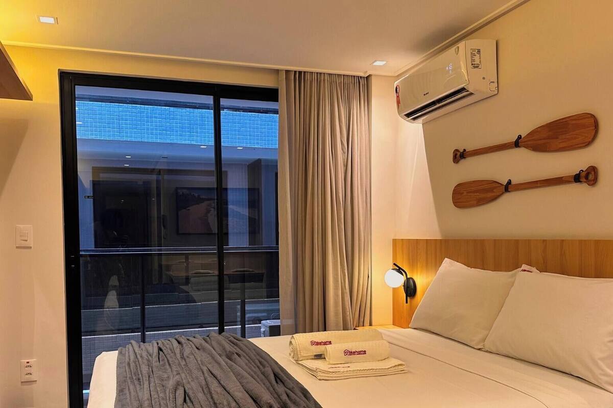 Habitación de hotel con cama, televisión, aire acondicionado, ventana con cortinas y vista al exterior.