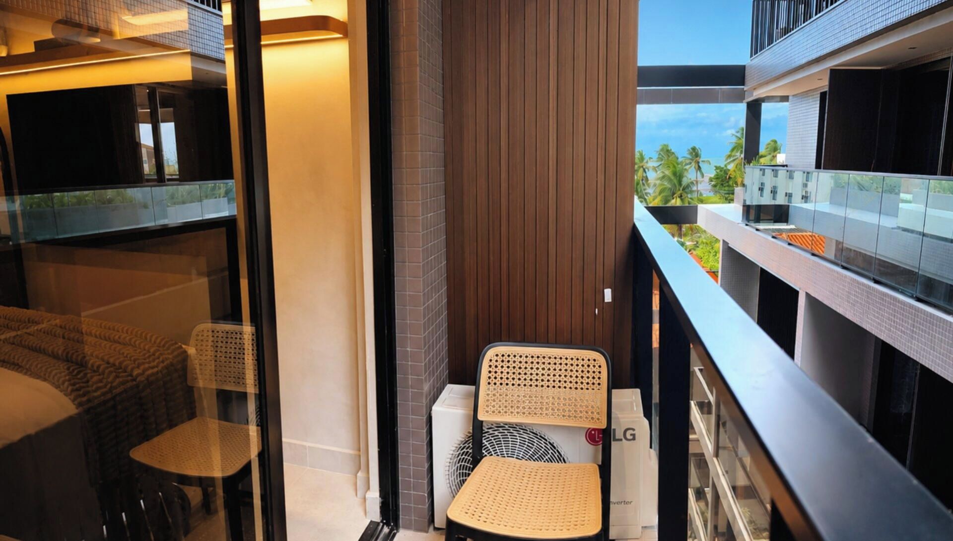 A balcony with a wicker chair, a small table, and a white LG inverter.