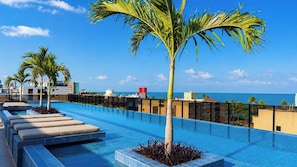 A rooftop infinity pool with palm trees, a clear sky, and a view of the ocean. - Hit Cabo Branco IV - LikeHome (João Pessoa)