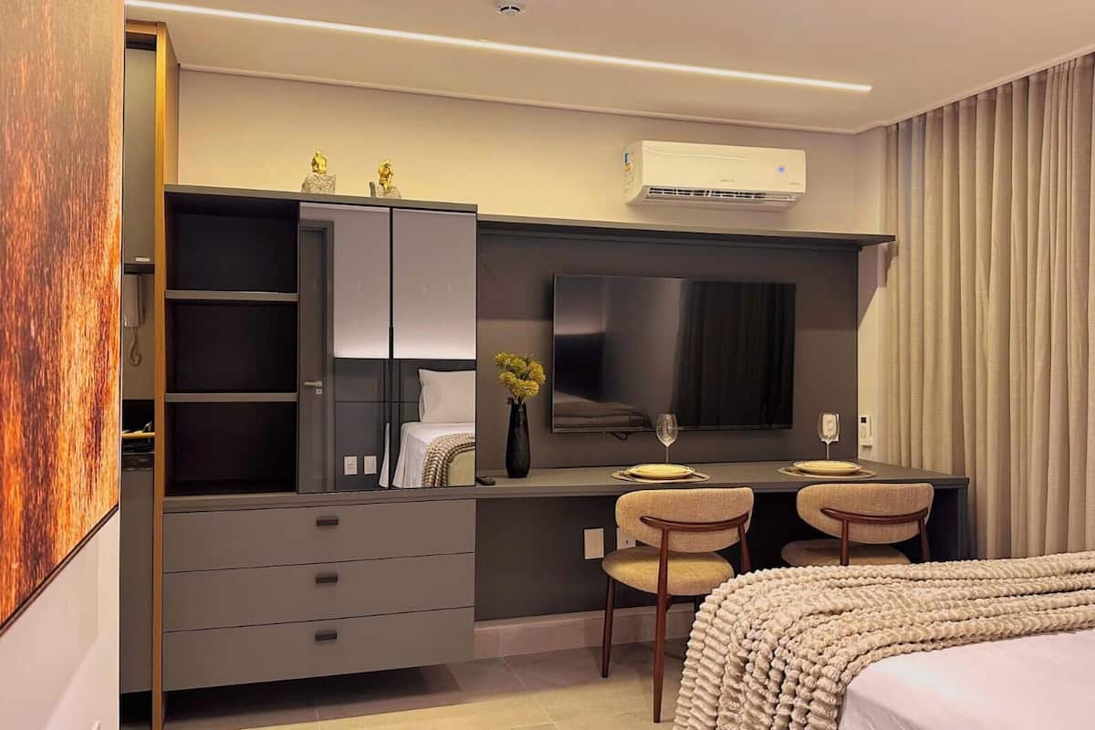 Una habitación de hotel moderna con una cama, un escritorio con dos sillas, un televisor de pantalla plana grande, un armario y un equipo de aire acondicionado.