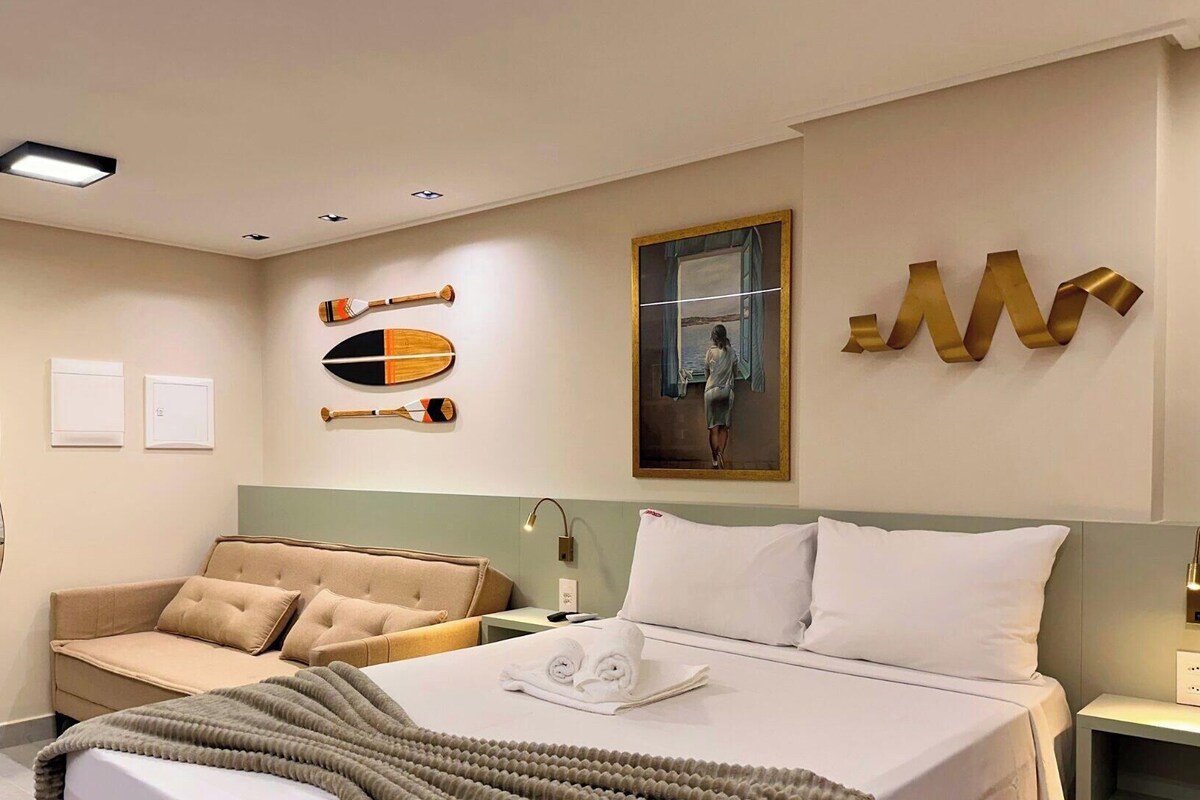 A hotel room with a bed, a sofa, a mirror, a painting, and a wall with decorative items.