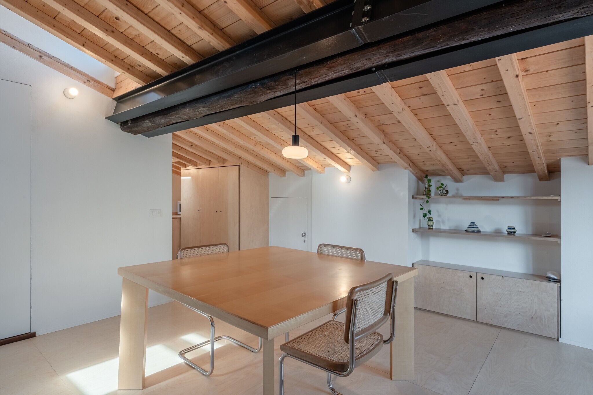Une cuisine moderne avec des poutres en bois, une table à manger en bois et un luminaire suspendu.