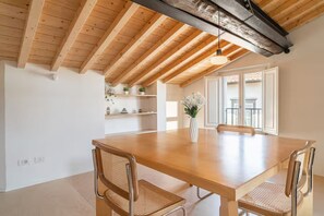 A spacious dining area with a wooden table and chairs, a hanging light fixture, and a view of the outside through large windows. - Nami House – Modern Comfort in the Heart of Lucca (Lucca)