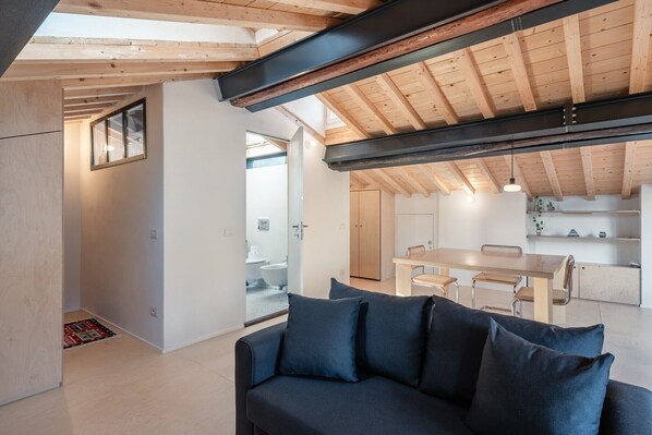 A modern interior with a wooden ceiling, a sofa, a dining table, and a kitchen area. - Nami House – Modern Comfort in the Heart of Lucca (Lucca)