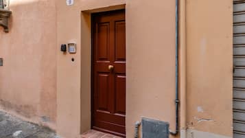 Une porte marron avec le chiffre « 9 » au-dessus, une petite fenêtre avec une grille en métal et un coffret de raccordement électrique au sol.