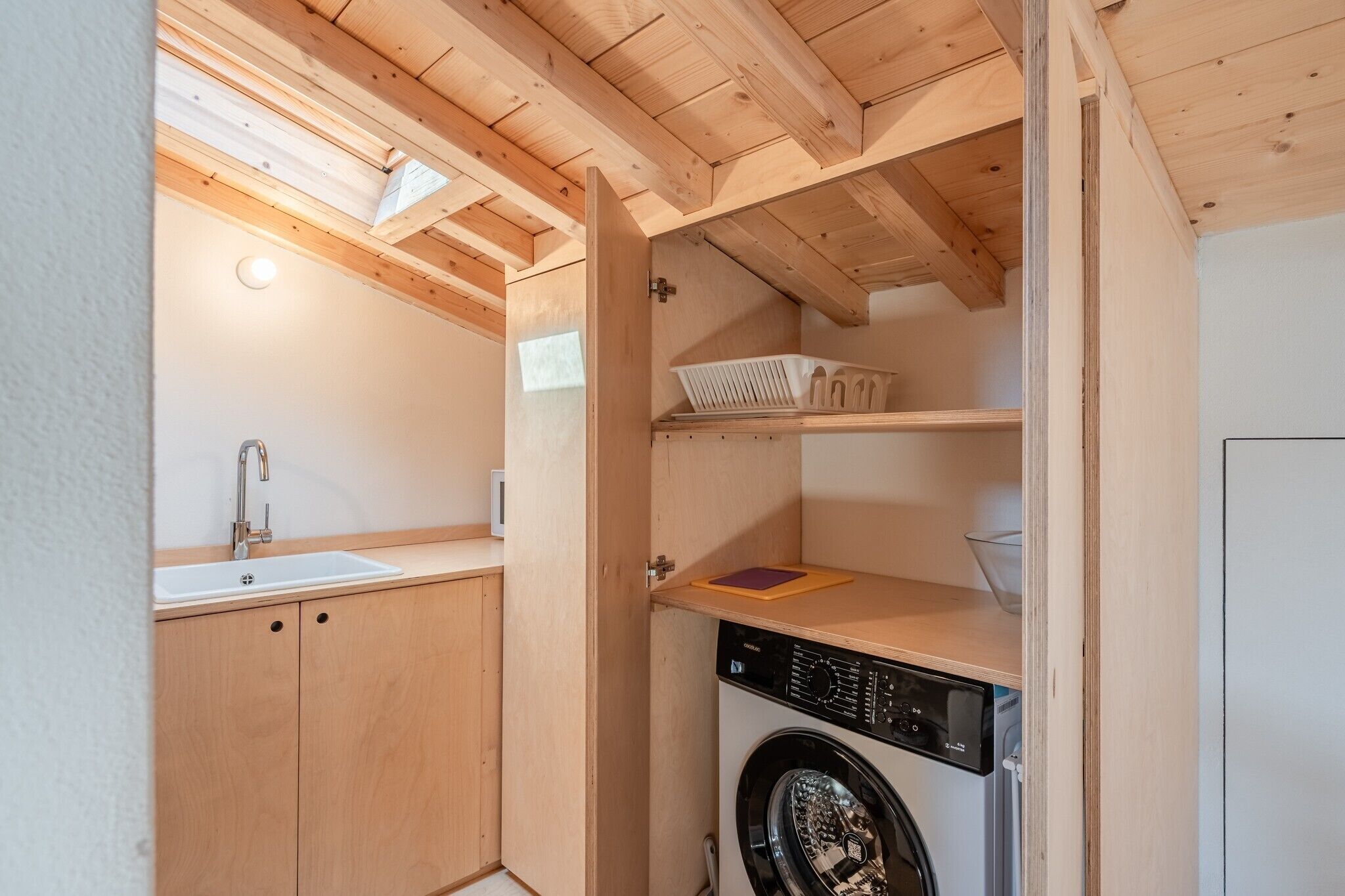 Une petite buanderie équipée d’un lave-linge, d’un évier et d’armoires en bois.