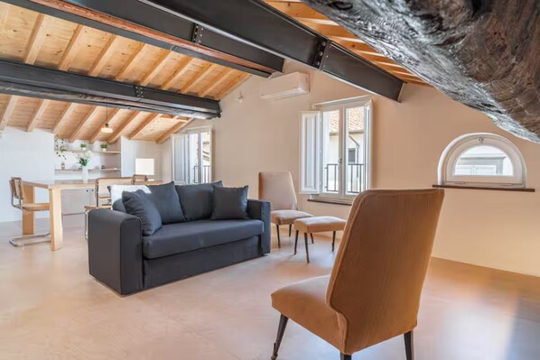 A spacious living area with a high ceiling, a sofa, a chair, and a dining table. - Nami House – Modern Comfort in the Heart of Lucca (Lucca)