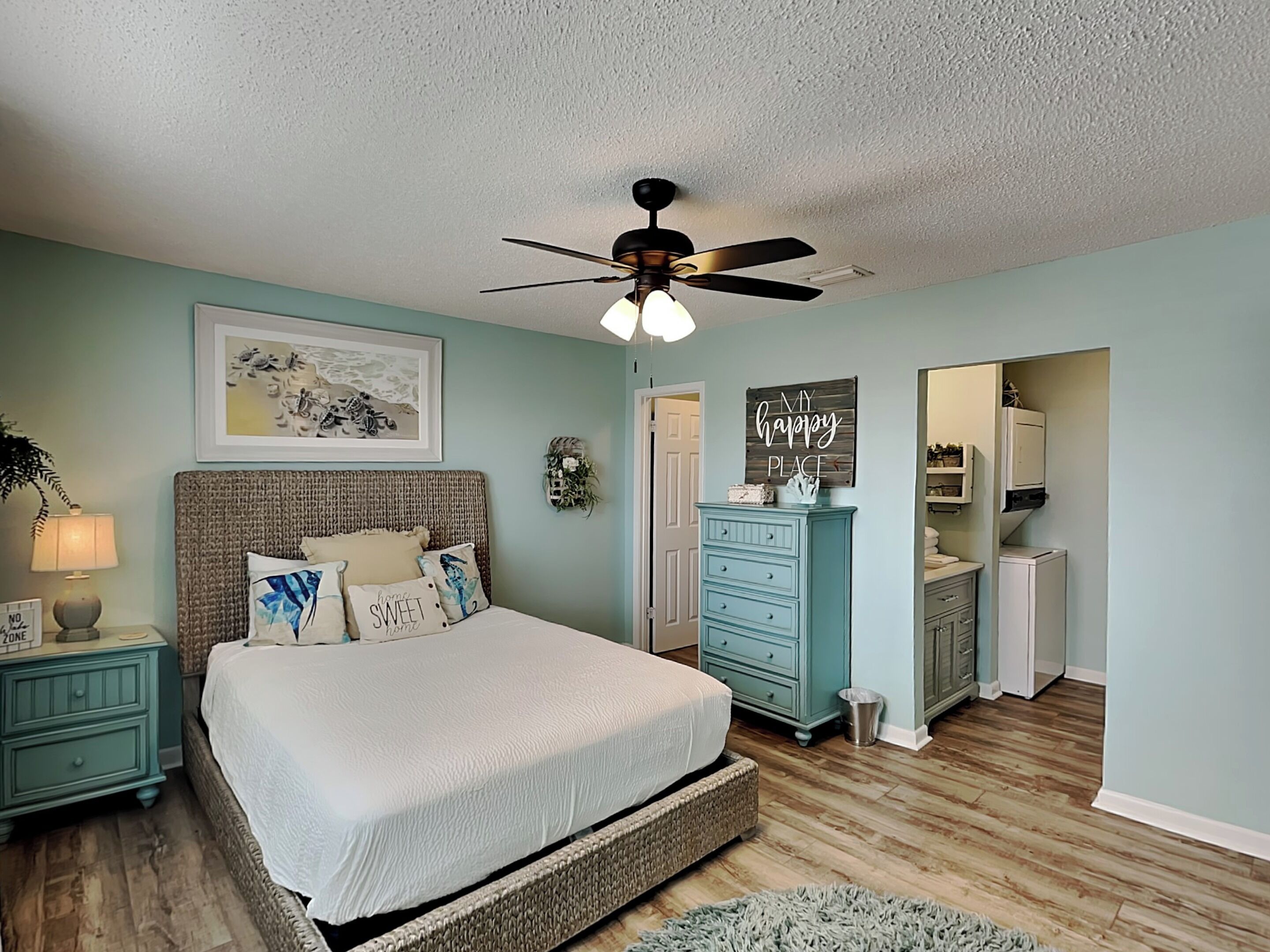 A bedroom with a bed, a ceiling fan, a dresser, and a small bathroom visible through an open door.