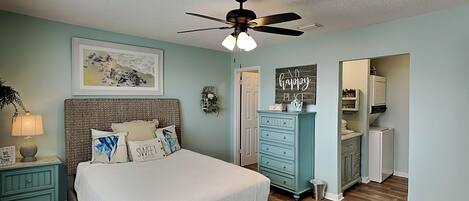 A bedroom with a bed, a ceiling fan, a dresser, and a small bathroom visible through an open door.