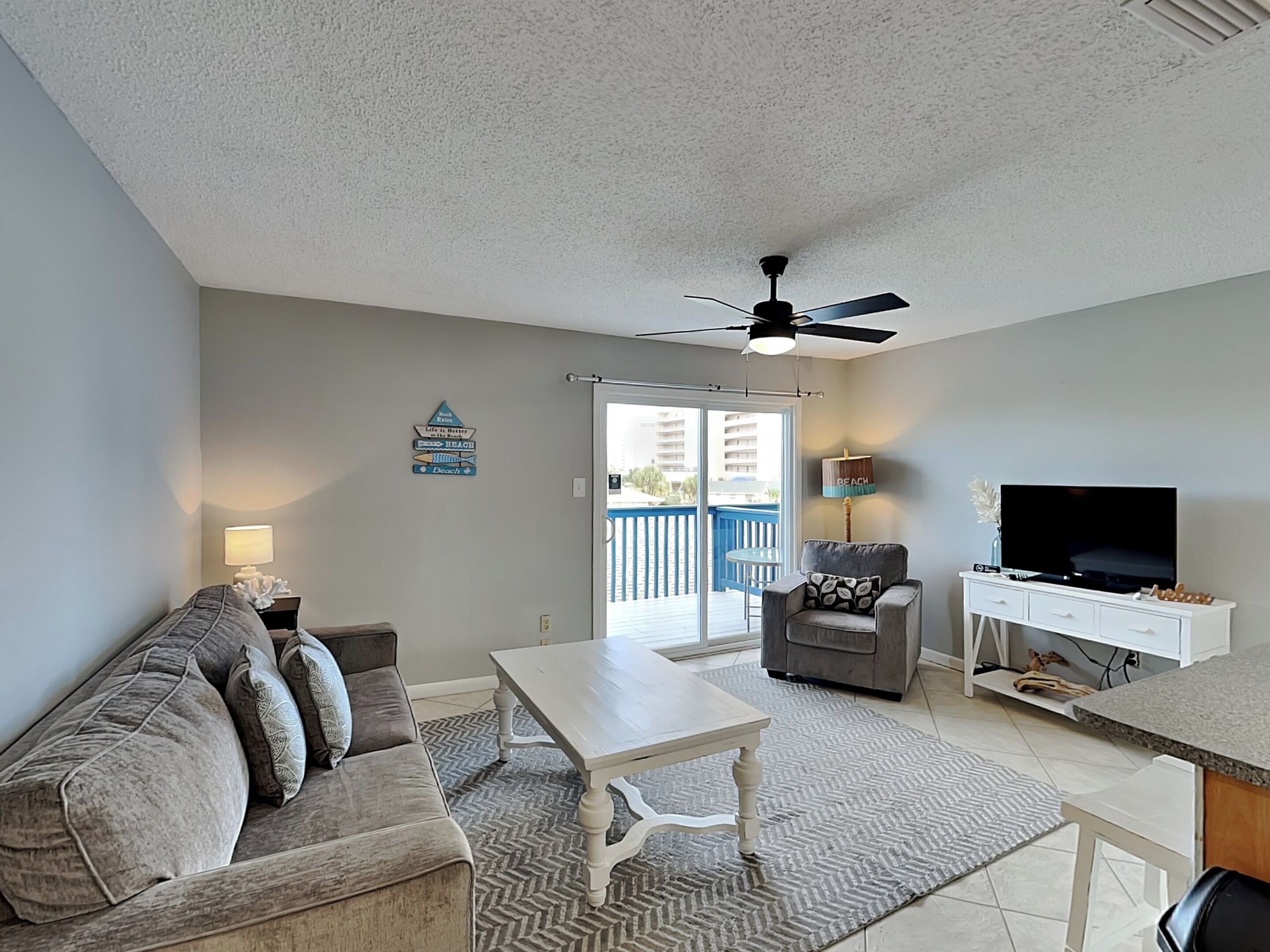 A living room with a sofa, a coffee table, a television, and a ceiling fan.