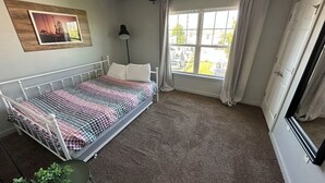 Een slaapkamer met een bed, een raam, een plant en een aan de muur hangend schilderij.