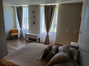 A bedroom with a bed, a chair, a small table, and a window with curtains.
