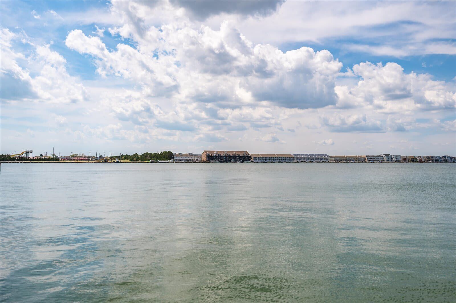 A waterfront view with buildings, a calm sea, and scattered clouds.