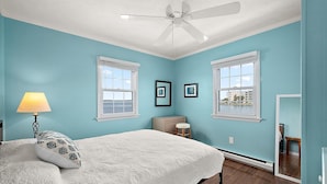 A bedroom with a bed, two windows, a ceiling fan, and a nightstand with a lamp. - Bayfront Condo with Great Location in Ocean City (Ocean City)