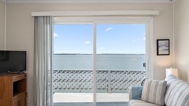 A room with a television, a sofa, a coffee table, and a view of the sea through a sliding door. - Bayfront Condo with Great Location in Ocean City (Ocean City)