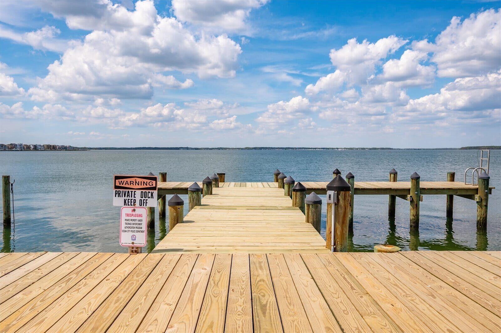 A wooden pier extending into calm water with a warning sign about private property.