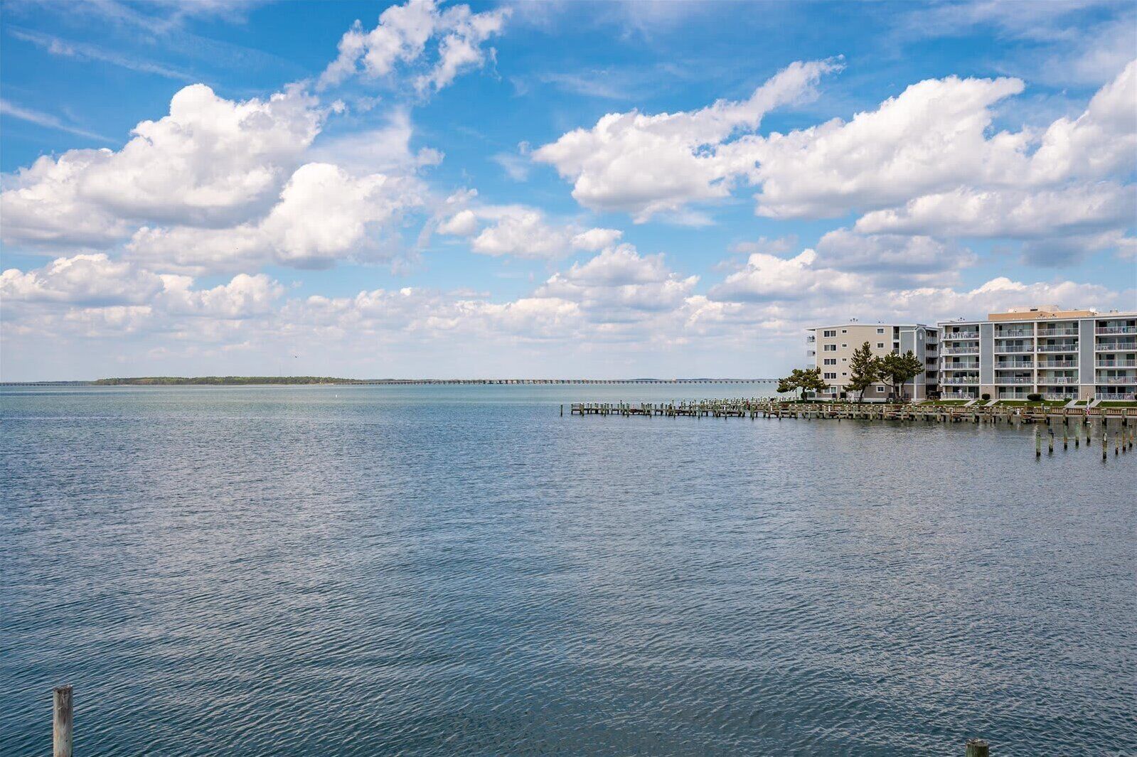 A waterfront hotel with a pier extending into the water, multiple balconies, and a clear view of the sea.