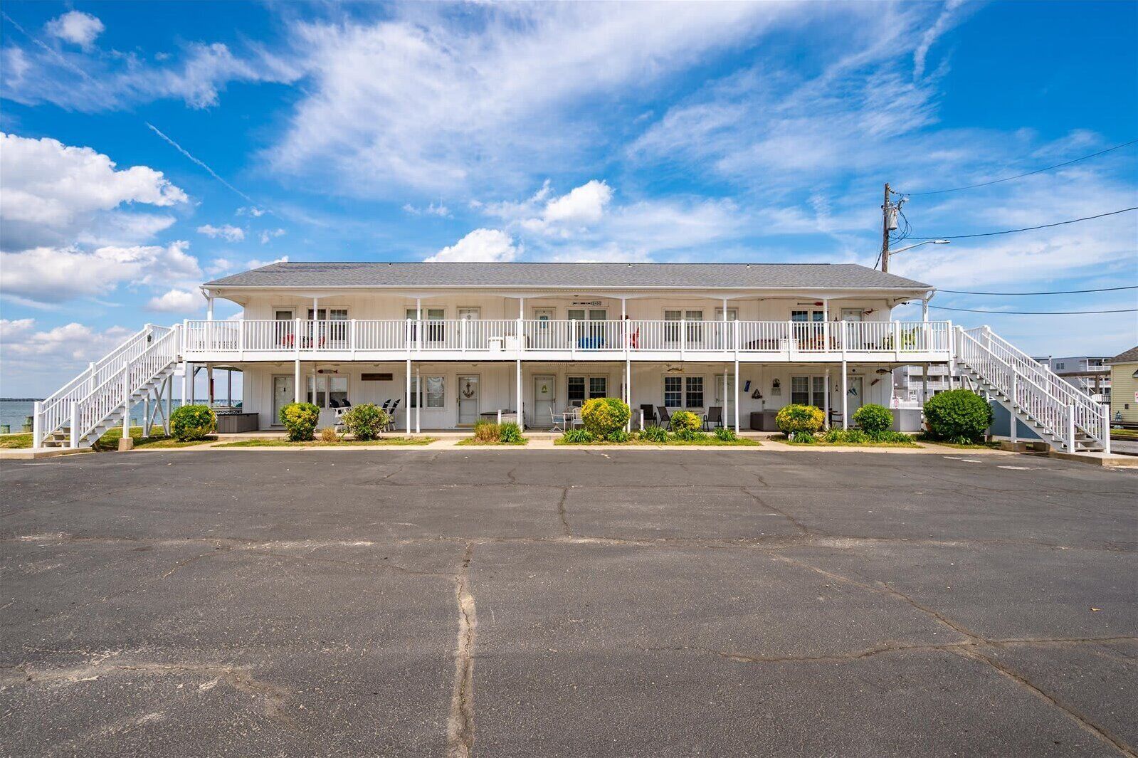 A two-story motel with a covered front porch, a parking lot, and a view of the water.