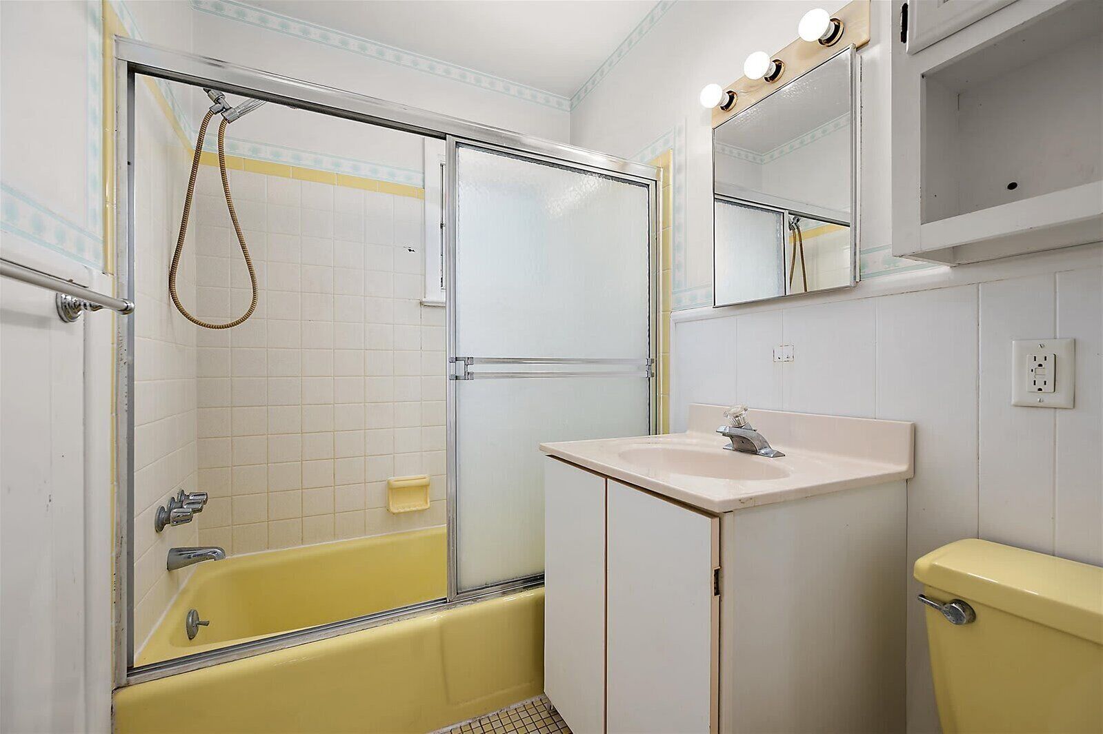A bathroom with a yellow bathtub, a white sink, and a mirror with lights.
