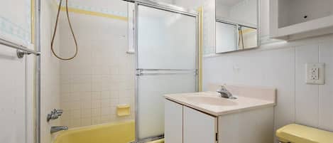 A bathroom with a yellow bathtub, a white sink, and a mirror with lights.