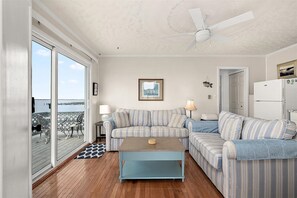 Ein Wohnzimmer mit einer Couch, einem Couchtisch, einem Deckenventilator, einem Kühlschrank und Blick auf den Ozean.