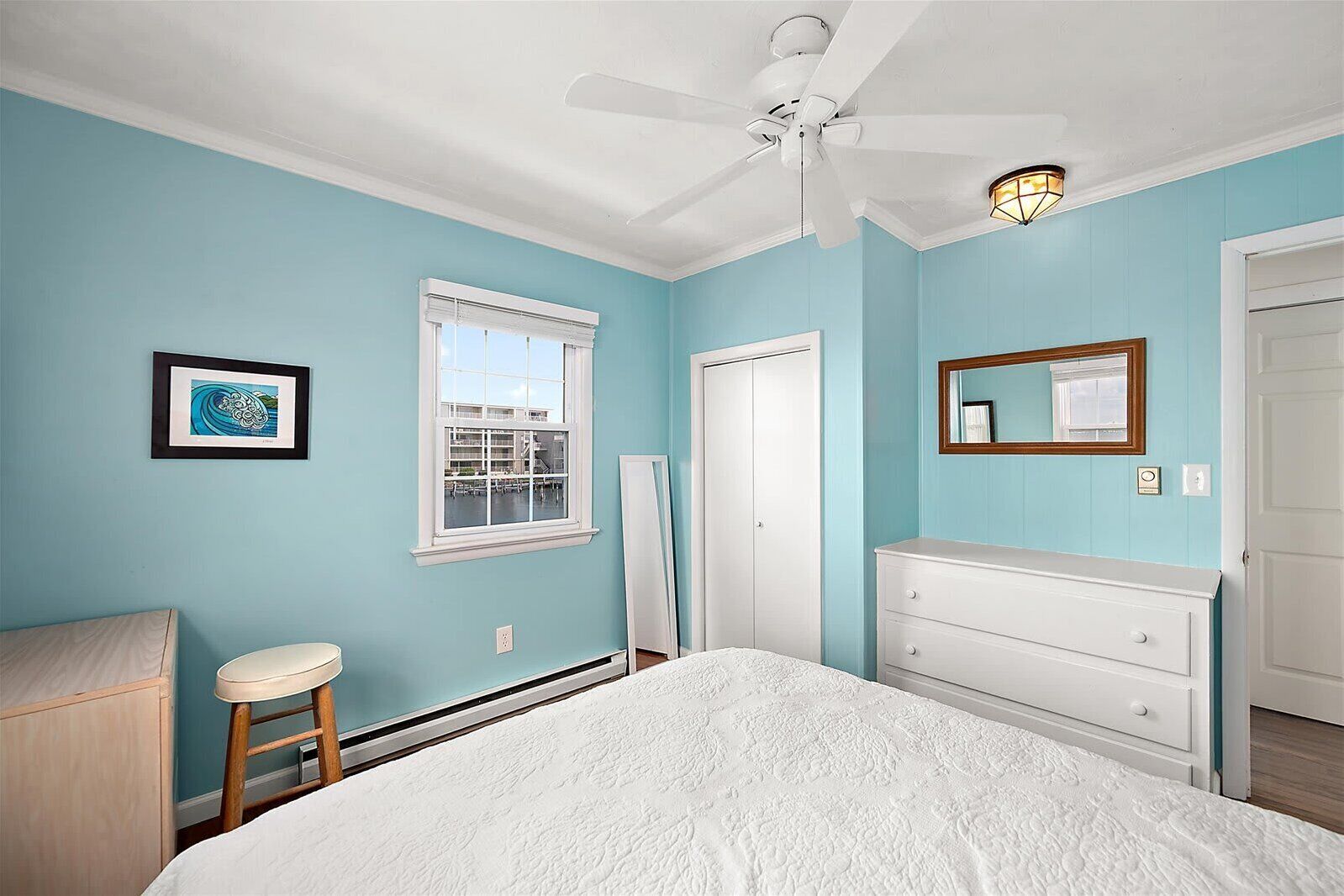 Un dormitorio con cama, cómoda, espejo, ventilador de techo y ventana.