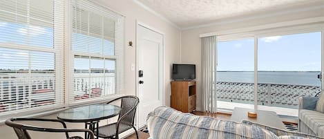 Una habitación con balcón, televisión, sofá y mesa de comedor.
